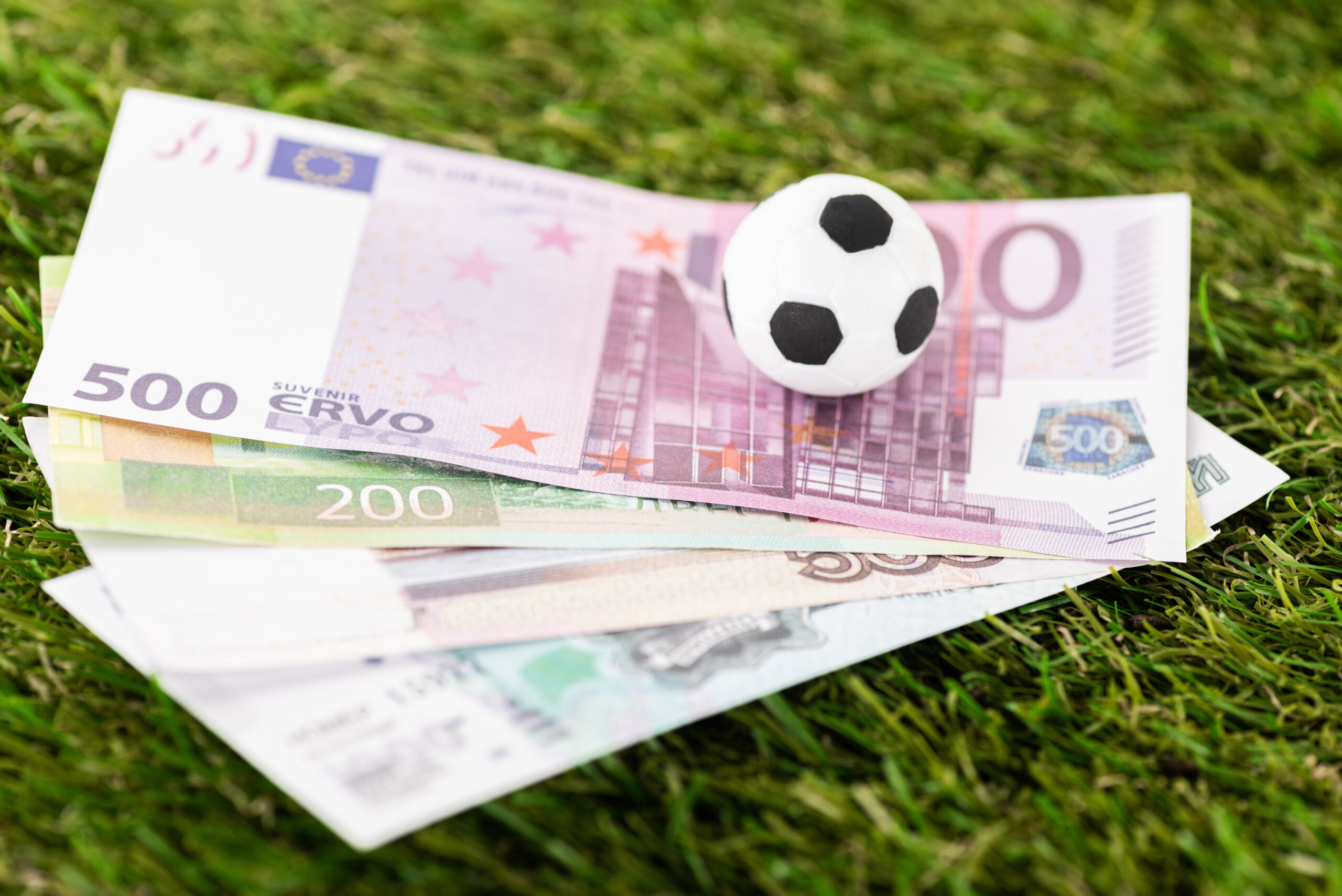 selective focus of toy soccer ball and euro banknotes on green grass, sports betting concept